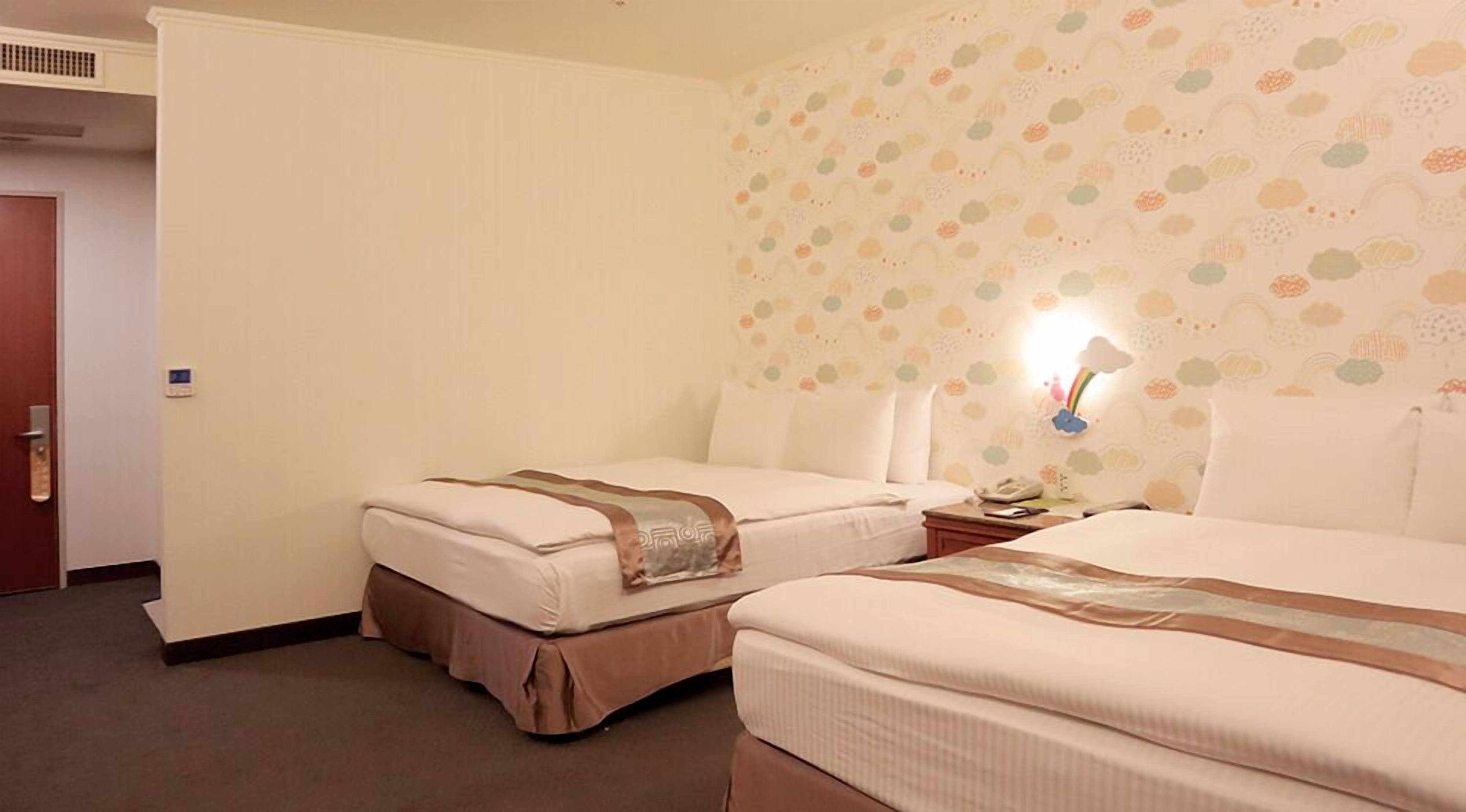 A hotel room with two beds, a nightstand, a lamp, and a wall with a floral pattern.