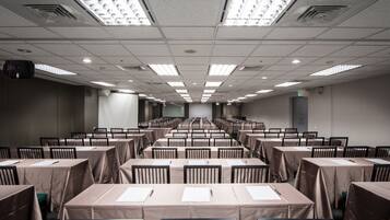 A conference room with rows of tables and chairs, equipped with ceiling lights and a projector.