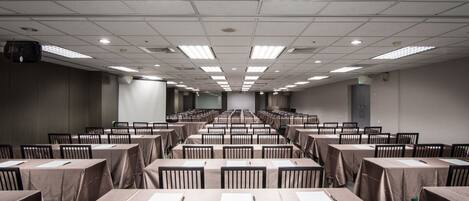 A conference room with rows of tables and chairs, equipped with ceiling lights and a projector.