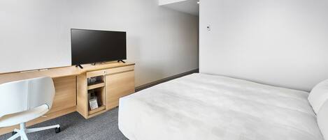 A hotel room with a bed, a desk with a flat-screen TV, a chair, and a carpeted floor.