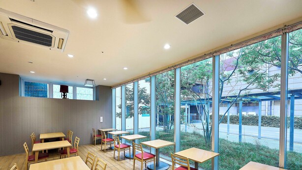 L’intérieur d’un restaurant avec des tables et des chaises en bois, de grandes fenêtres et une vue sur l’extérieur.