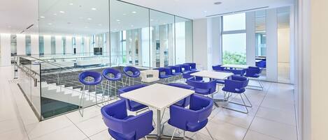 Un espace intérieur moderne et bien éclairé, avec des murs en verre, des chaises bleues et des tables blanches.