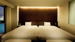 Habitación de hotel con una cama grande, una mesita de noche, una ventana con cortinas y vistas a la ciudad.