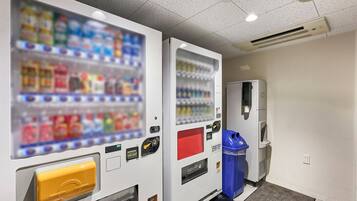 A vending machine area with a beverage dispenser and a trash bin.