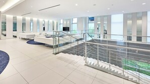 Un vestíbulo espacioso con una escalera moderna, zonas de estar y grandes ventanales con vistas al exterior.