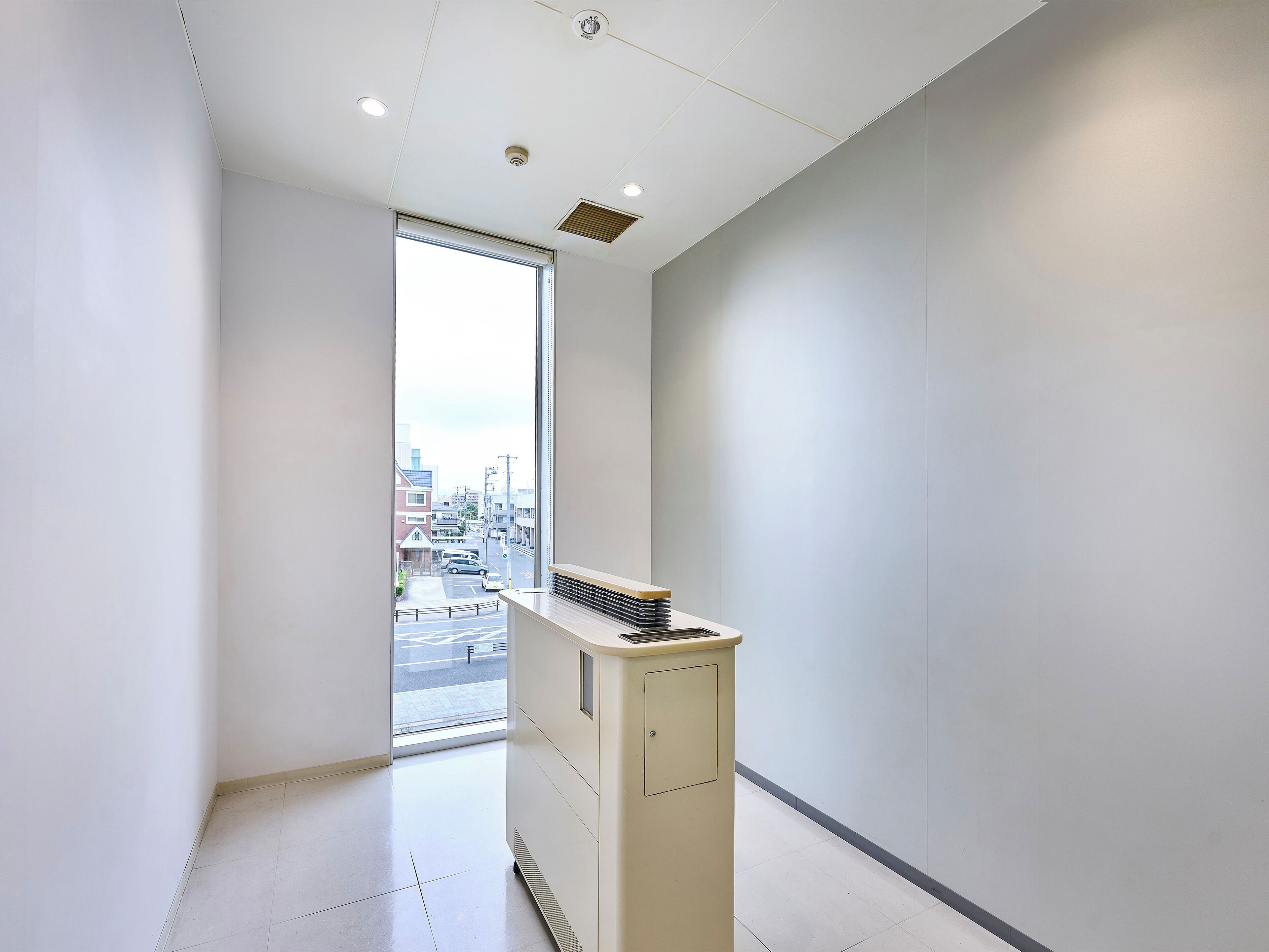 Corredor moderno e minimalista com uma grande janela que oferece vista da cidade, um pequeno radiador e interior limpo e branco.