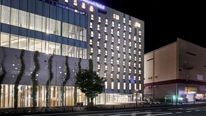 Un hotel moderno con fachada de vidrio, señalización iluminada y zona de estacionamiento.