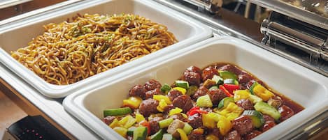 A buffet with various dishes including noodles and a meat dish with vegetables.