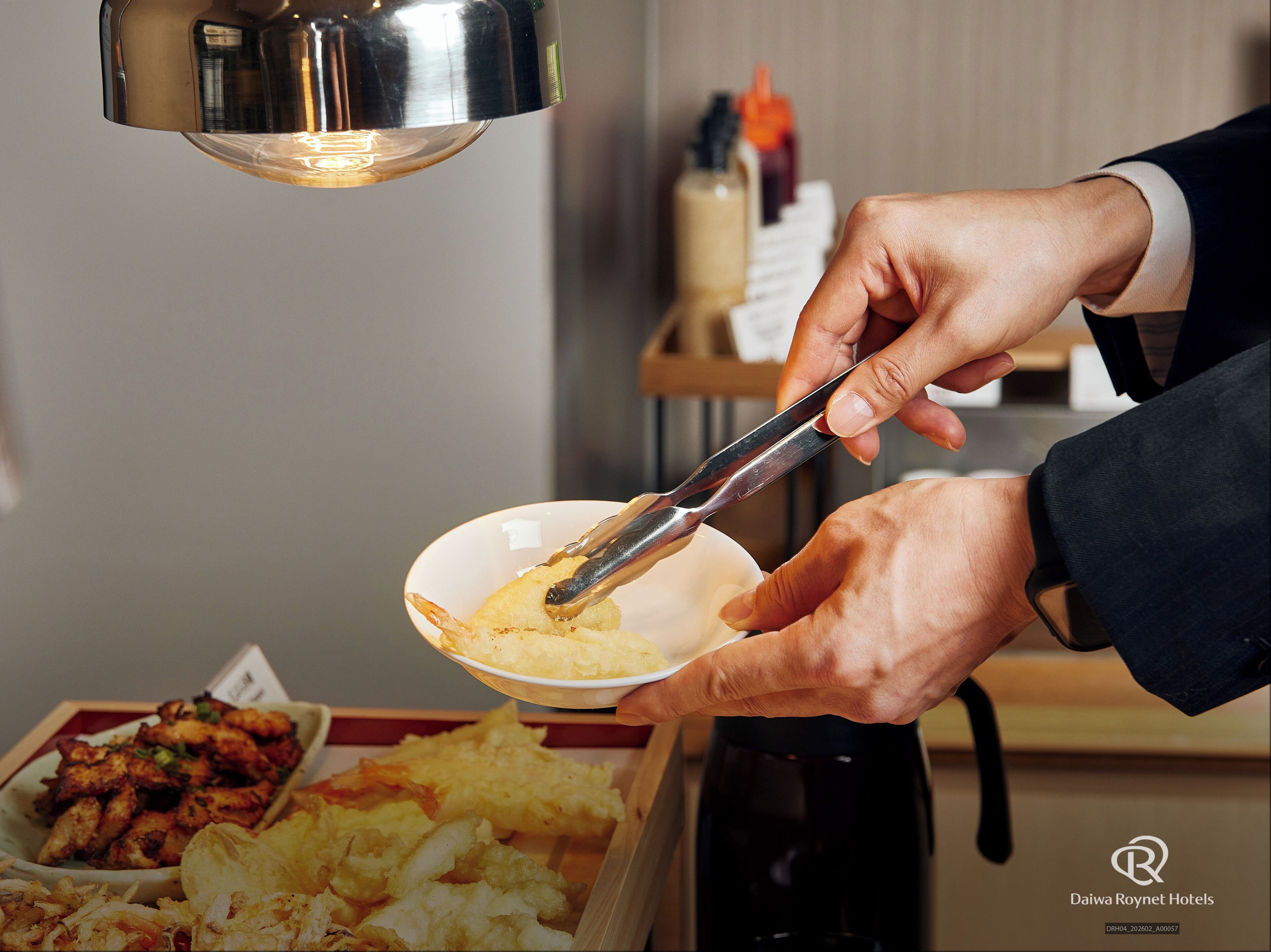 A person using tongs to serve food from a bowl.