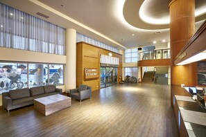 A spacious lobby with a wooden floor, a grey sofa, a small armchair, and a reception desk. - Ho Fong Business Stay (Taichung)