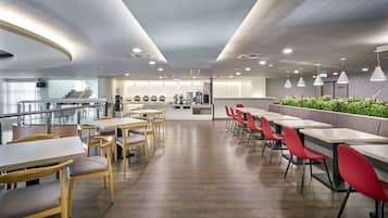 En moderne restaurant med træ- og røde stole, et køkkenområde samt udsigt til øvre etage.