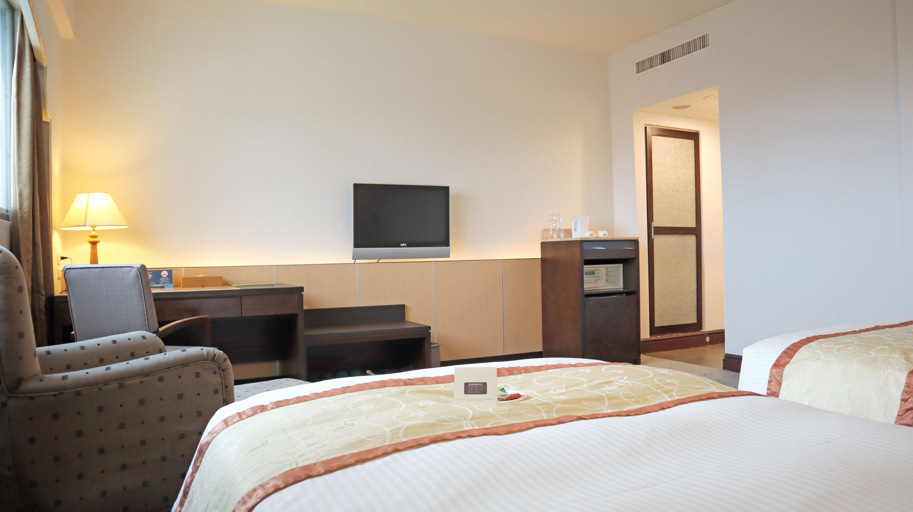 A hotel room with a bed, a desk, a chair, a television, and a minibar.