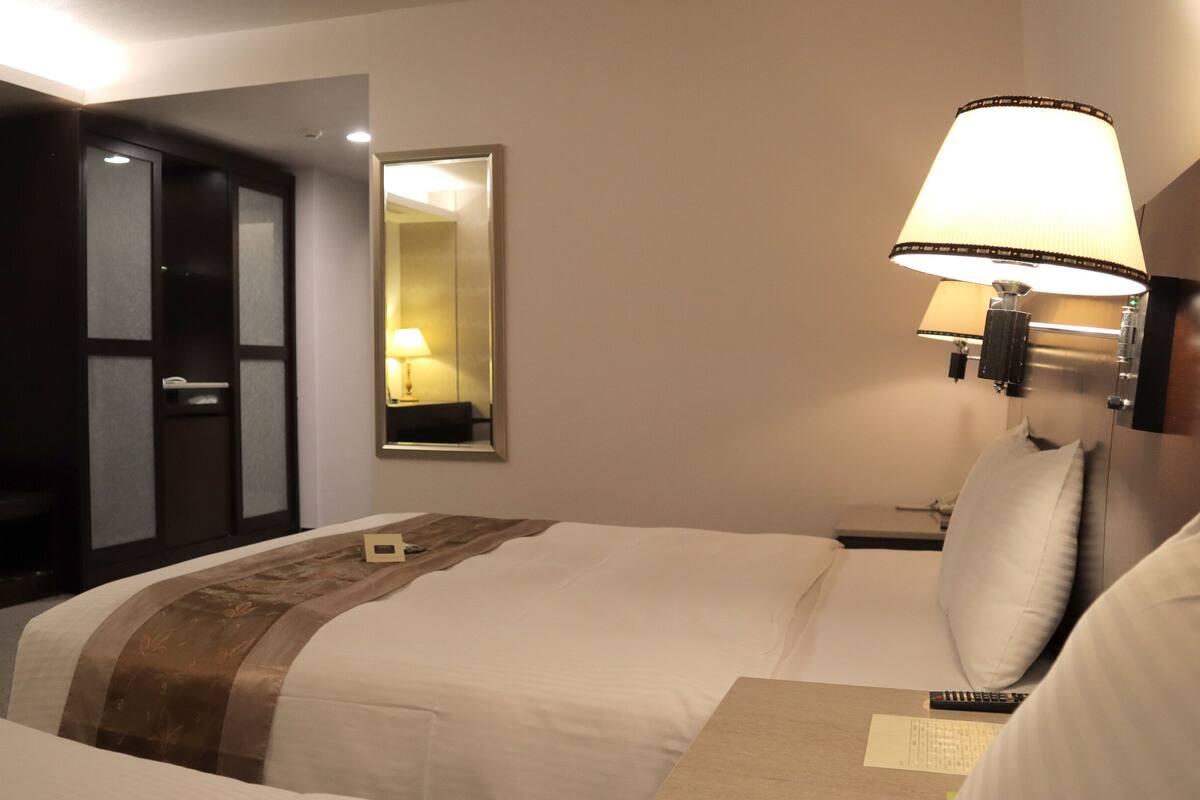 A hotel room with a bed, a nightstand, a lamp, a mirror, and a TV on the wall.