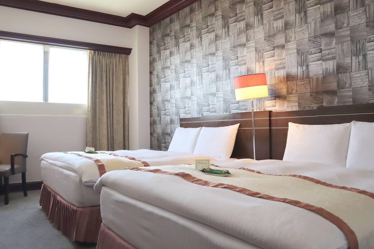 A hotel room with two beds, a desk, and a chair.