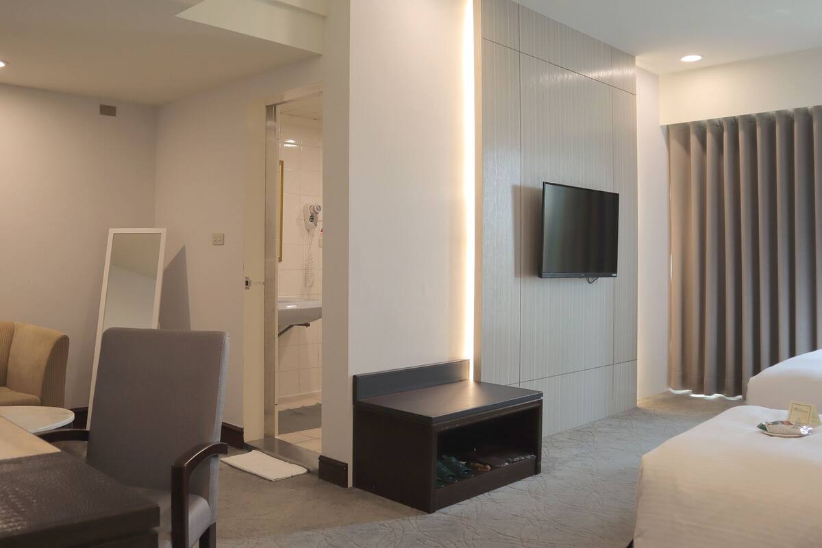 A modern hotel room with a sofa, a chair, a TV, a small table, and a bed.
