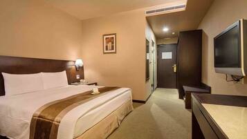 A hotel room with a large bed, a bedside table with a lamp, a television, and a door leading to a hallway.
