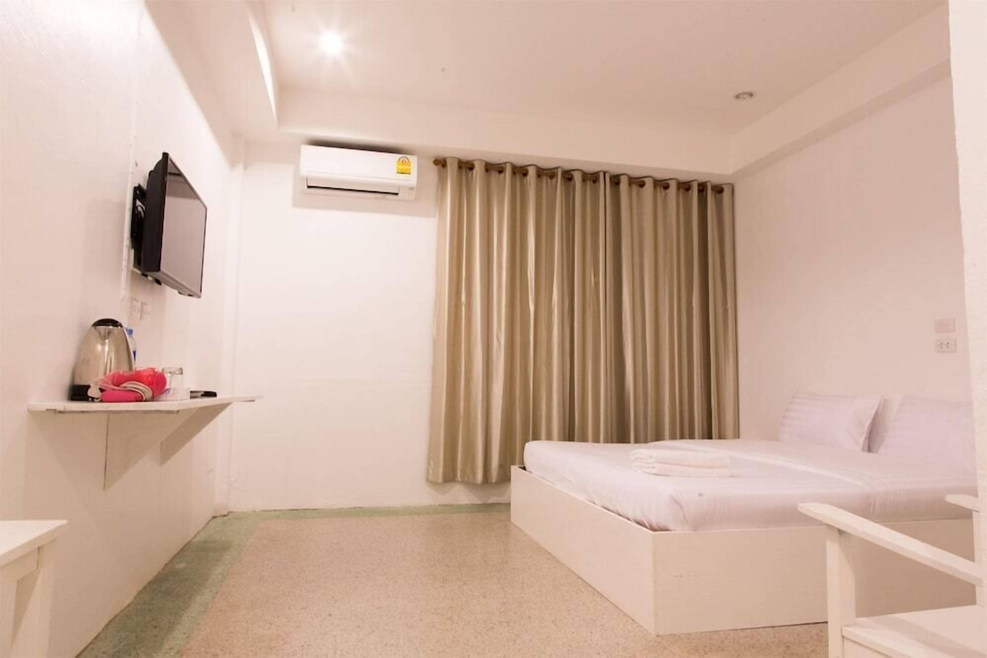 A hotel room with a bed, a TV mounted on the wall, an air conditioning unit, and a curtain.