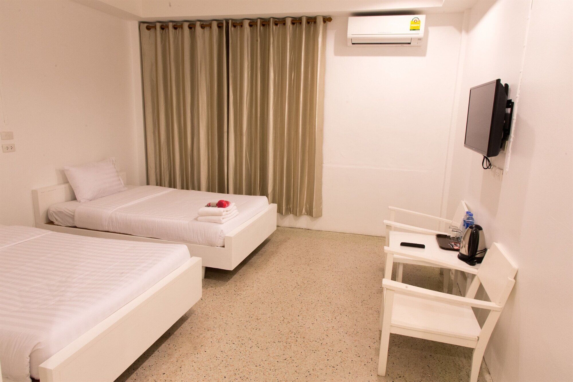 A hotel room with two beds, a desk, a chair, an air conditioning unit, and a television.