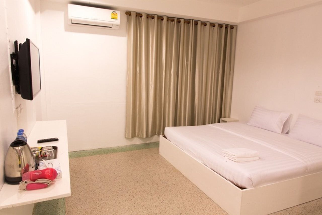 Une chambre d’hôtel avec un lit, une table de chevet avec une bouilloire, une bouteille d’eau et un objet rouge.