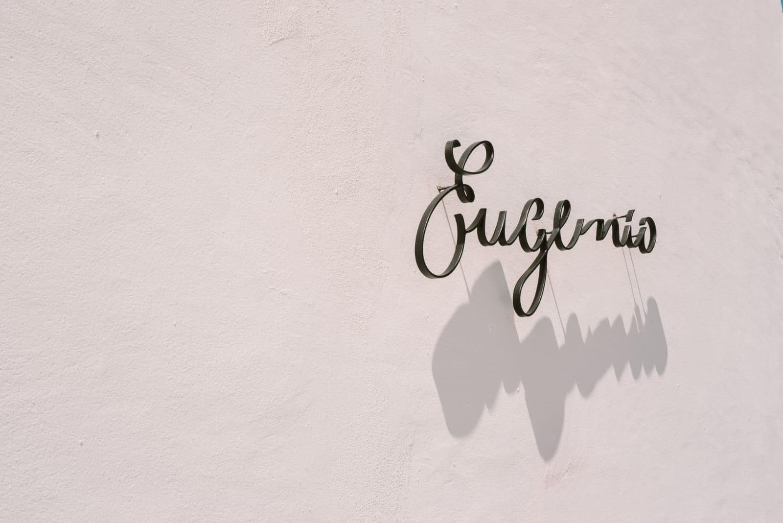 A wall with the word 'Cuneglio' in a cursive font and a shadow of a person.