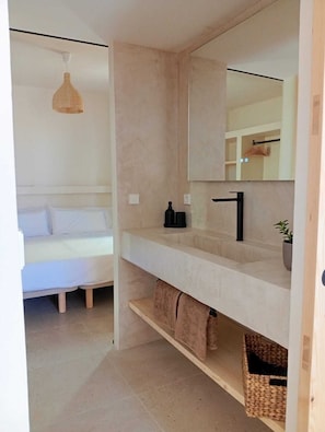 A modern bathroom with a large mirror, a white sink, and a bed with white bedding. - Apartamentos Eugenio by Formentera Passport (Formentera)