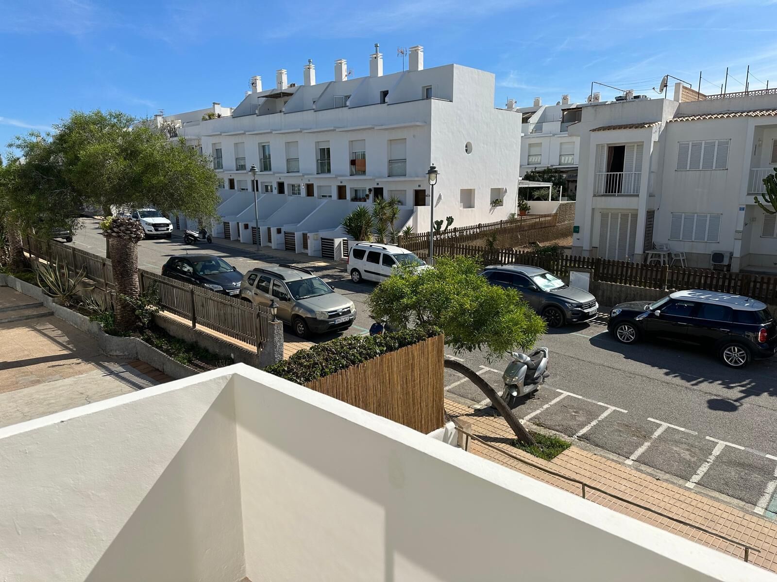 A residential street with white buildings, parked cars, and a clear sky.