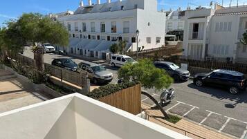 A residential street with white buildings, parked cars, and a clear sky.