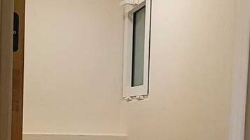 A small, narrow bathroom with a toilet, a small window, and a wall-mounted flush handle.