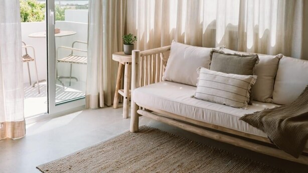 Una habitación con sofá, una mesita, una planta en maceta y vistas al exterior.