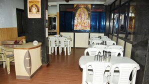 Un restaurante con sillas y mesas de plástico blanco, una barra de madera y un gran mural religioso en la pared.