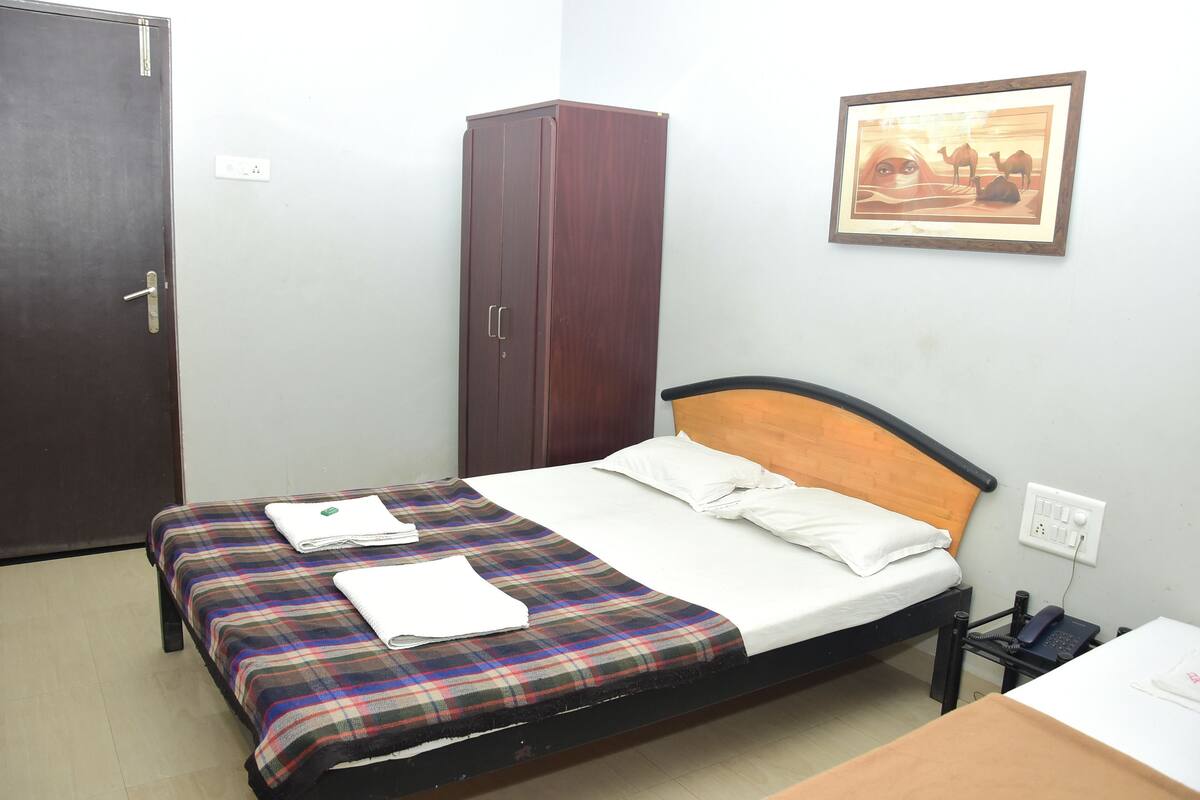 A single bed with a plaid bedspread, a wooden headboard, and a bedside table with a phone.