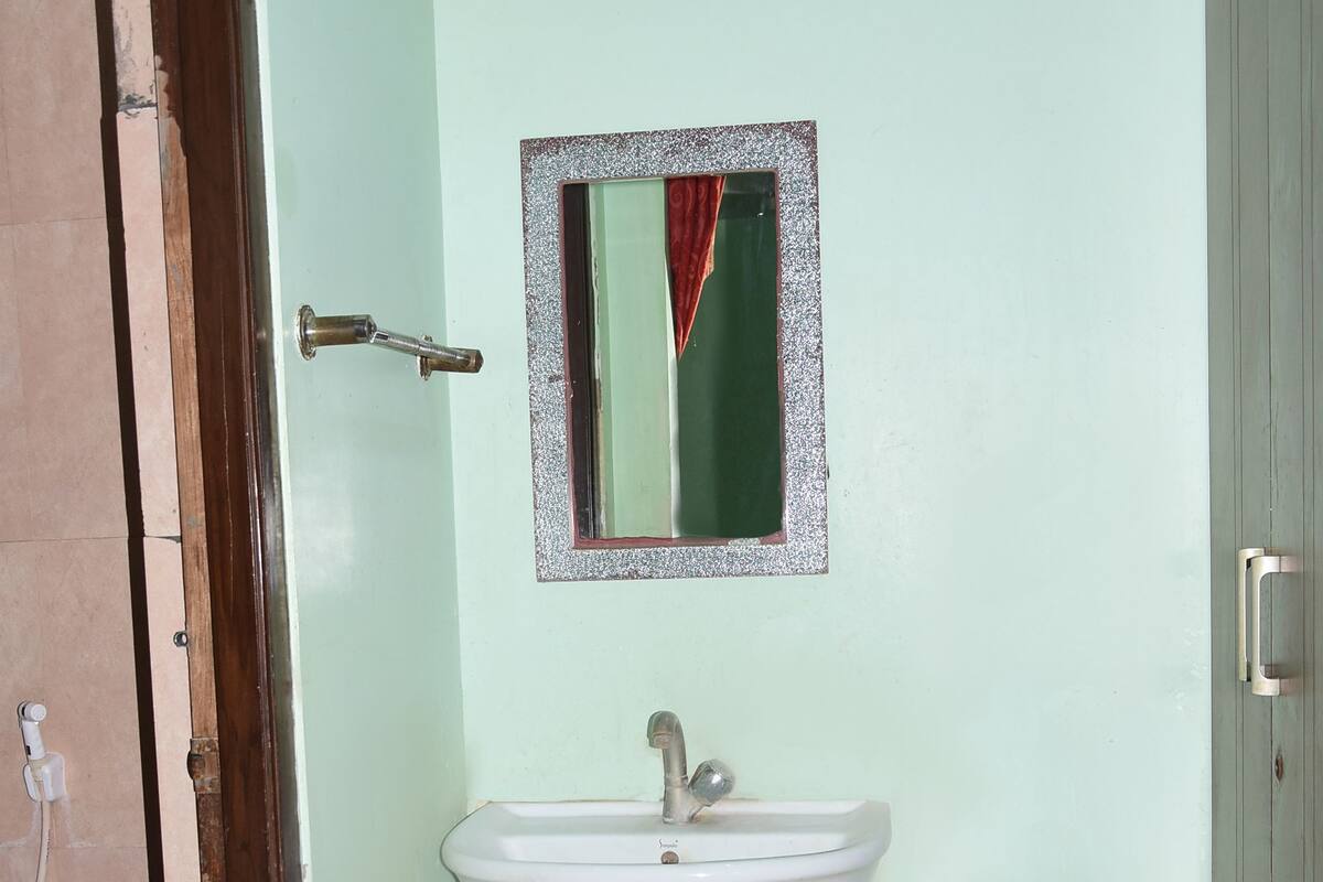 A bathroom with a white sink, a blue bucket, and a mirror with a red curtain.