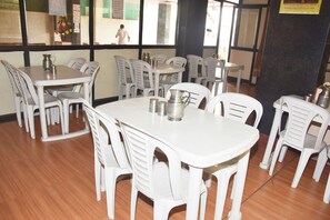 A restaurant interior with white plastic chairs and tables, a wooden floor, and a view of the street outside.