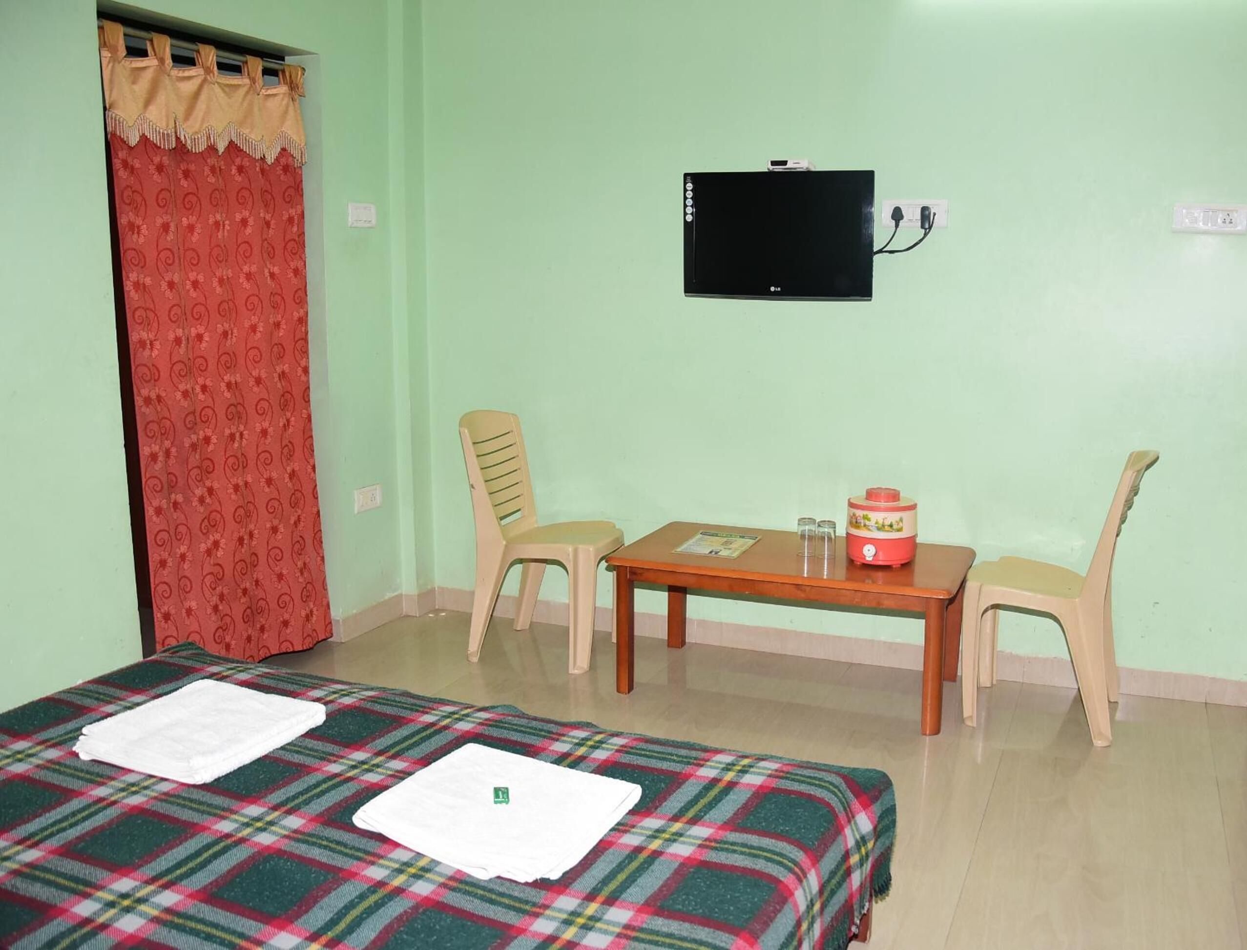 Quarto com cama, duas cadeiras, uma mesa pequena, televisão e cortina vermelha.