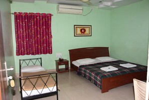 A bedroom with a bed, a nightstand, a chair, a window with curtains, and an air conditioning unit.