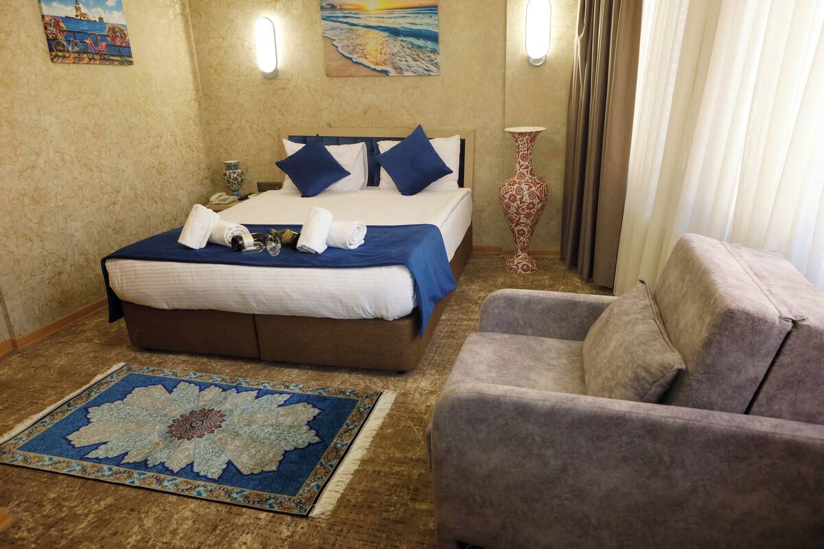 A hotel room with a bed, a chair, a rug, and artwork on the walls.