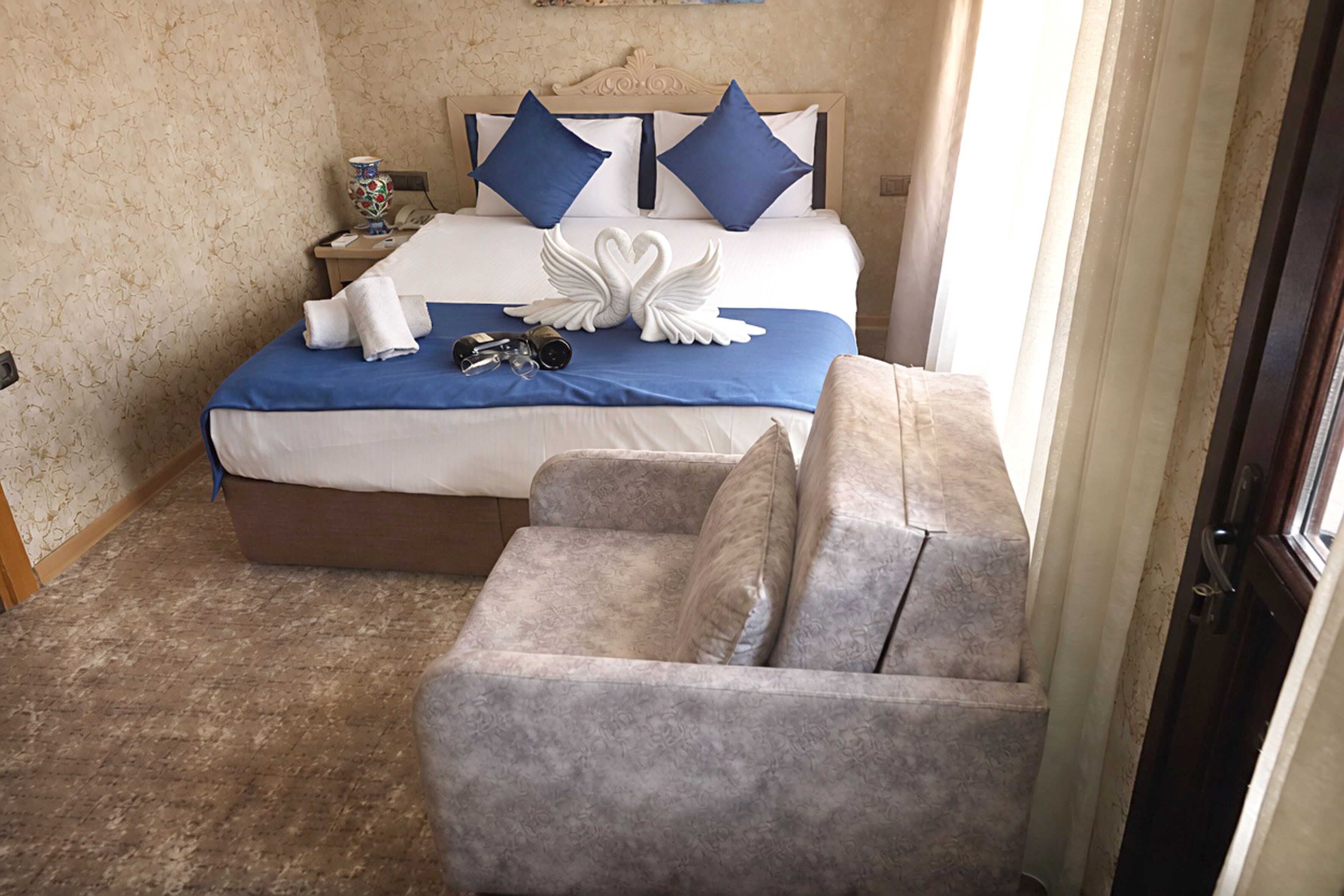 A hotel room with a bed, a nightstand with a lamp, a chair, and a decorative swan on the bed.