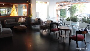 Un espacio interior moderno con un sofá, sillas y una mesita de centro. Se ve un ventanal con vistas a la vegetación.
