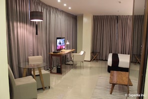 A modern hotel room with a flat-screen TV, a glass table, two chairs, a desk, and a bed.