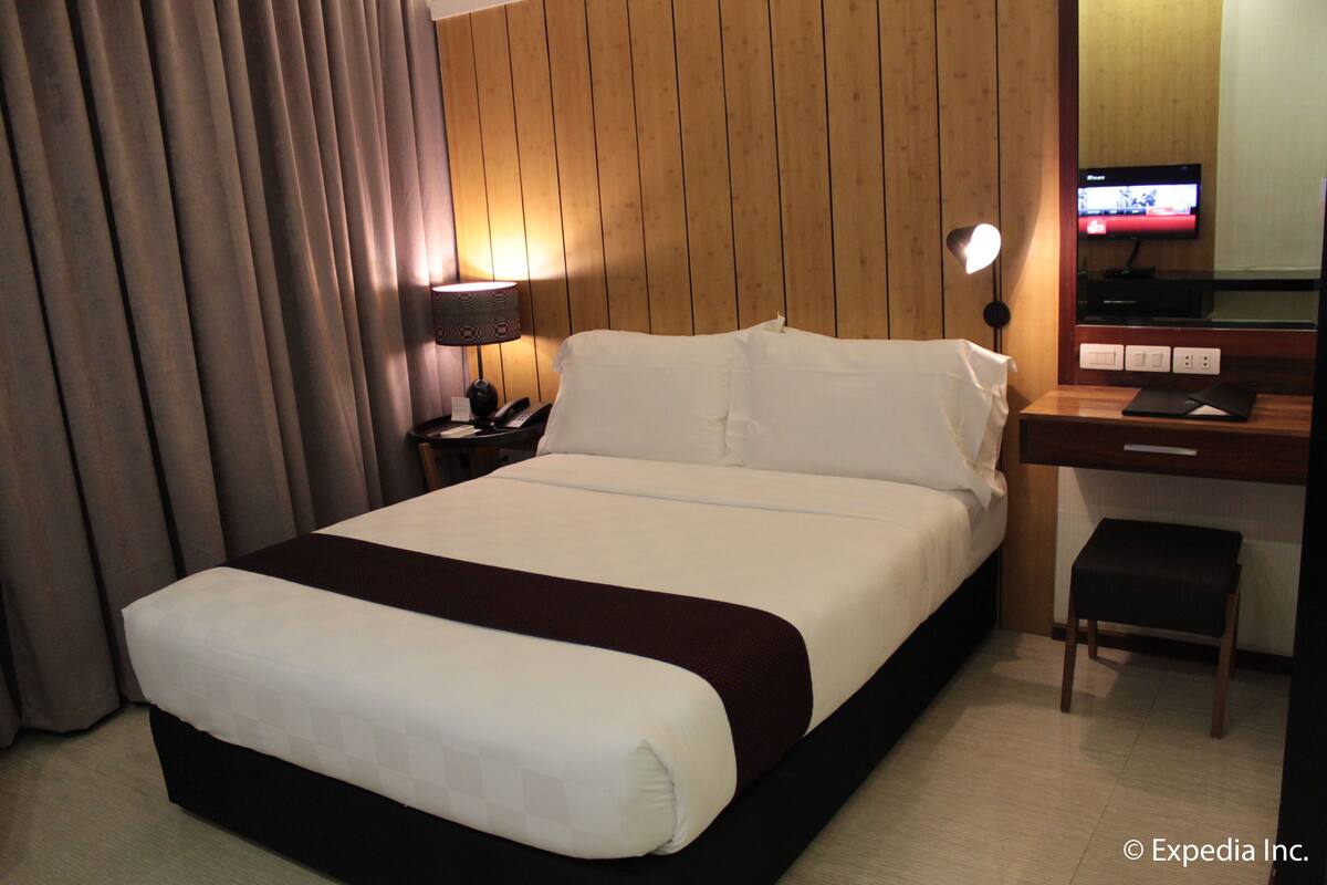 Ein Hotelzimmer mit einem großen Bett, einem Schreibtisch mit Stuhl, einem Fernseher und einer Lampe.