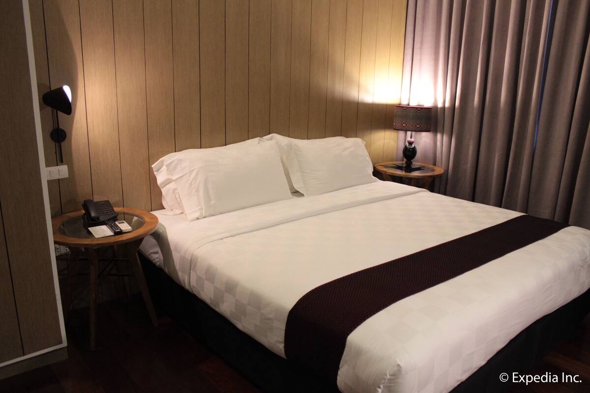Ein Hotelzimmer mit einem großen Bett, einem Nachttisch mit Lampe und einem Telefon.