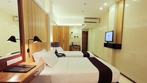 Habitación de hotel con dos camas, un escritorio con una computadora portátil, un televisor montado en la pared y una mesita con una tetera.