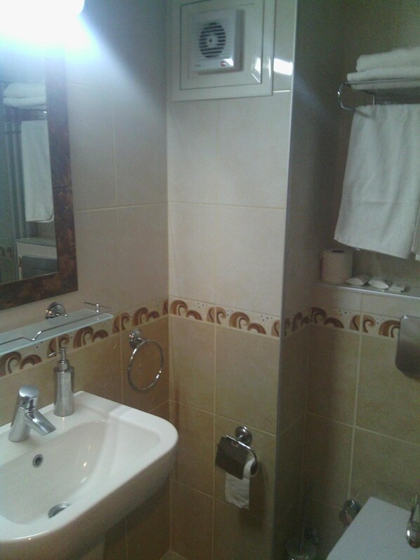 Un baño con lavamanos, espejo, toallero y dispensador de papel higiénico.