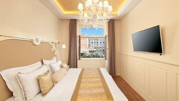 A hotel room with a large bed, a television on the wall, and a view of the city through the window.