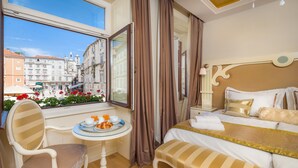 A hotel room with a bed, a chair, a small table with a tray of food, and a window offering a view of the city. - Piazza Heritage Hotel (Split)
