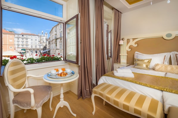 A hotel room with a bed, a chair, a small table with a tray of food, and a window offering a view of the city.