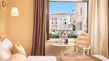 Habitación de hotel con cama, una silla, una mesa con un florero y vista a edificios a través del ventanal.
