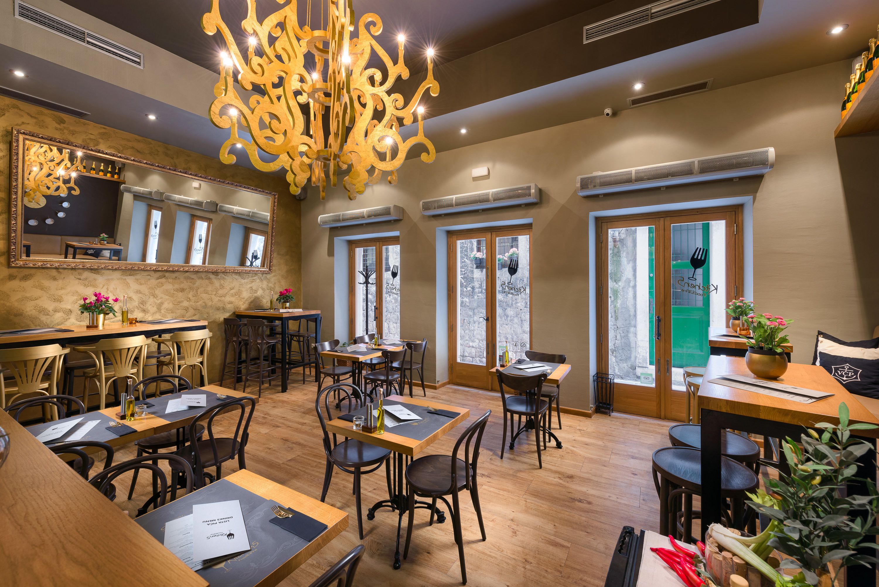 A restaurant with wooden tables and chairs, a chandelier, and large windows.