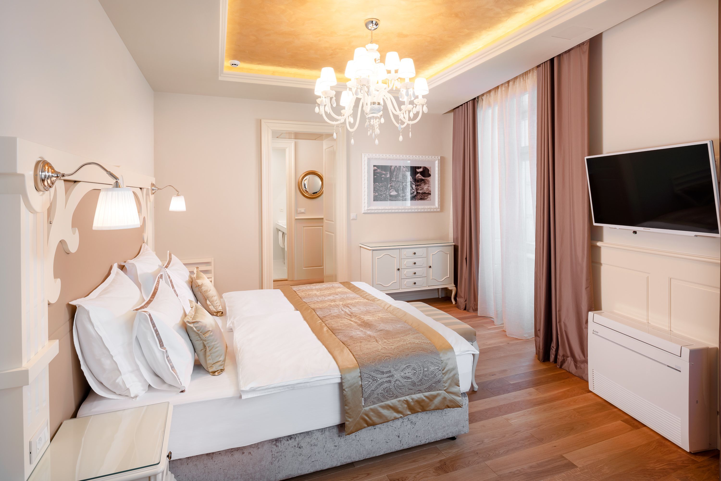 A modern bedroom with a large bed, a TV, a chandelier, and a dresser.