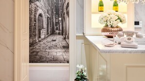 A hallway with a marble floor, a chandelier, a wall-mounted light fixture, and a display of champagne bottles. - Piazza Heritage Hotel (Split)